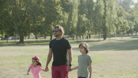 Handheld-shot-of-dad-with-disability-walking-with-kids-in-park